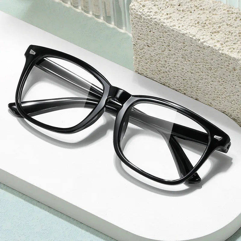 A pair of black anti-blue light gaming glasses resting on a white surface next to a textured block.