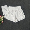 White women's high-waist yoga and fitness shorts laid flat on a dark gray surface next to pink and white tulips.