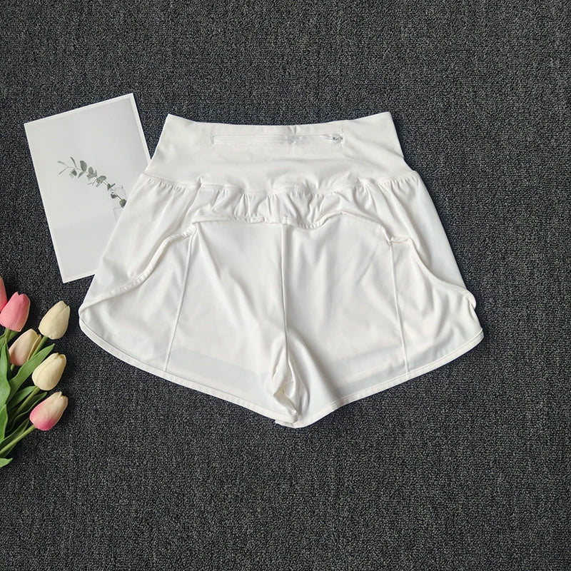 White women's high-waist yoga and fitness shorts laid flat on a dark gray surface next to pink and white tulips.