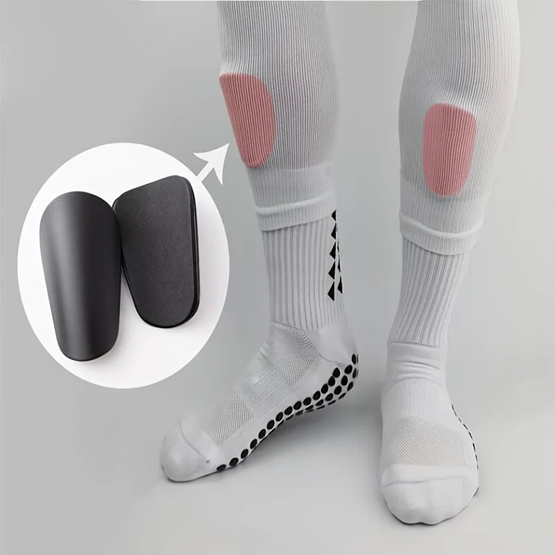 Un paire de protège-tibias de football blancs avec rembourrage rose sur une jambe, à côté de protections d'entraînement noire