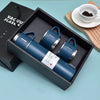 A dark blue vacuum flask in its box with a wooden board and a white cup of coffee.