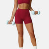 A woman wearing a maroon high-support sports bra and matching shorts, holding light dumbbells.