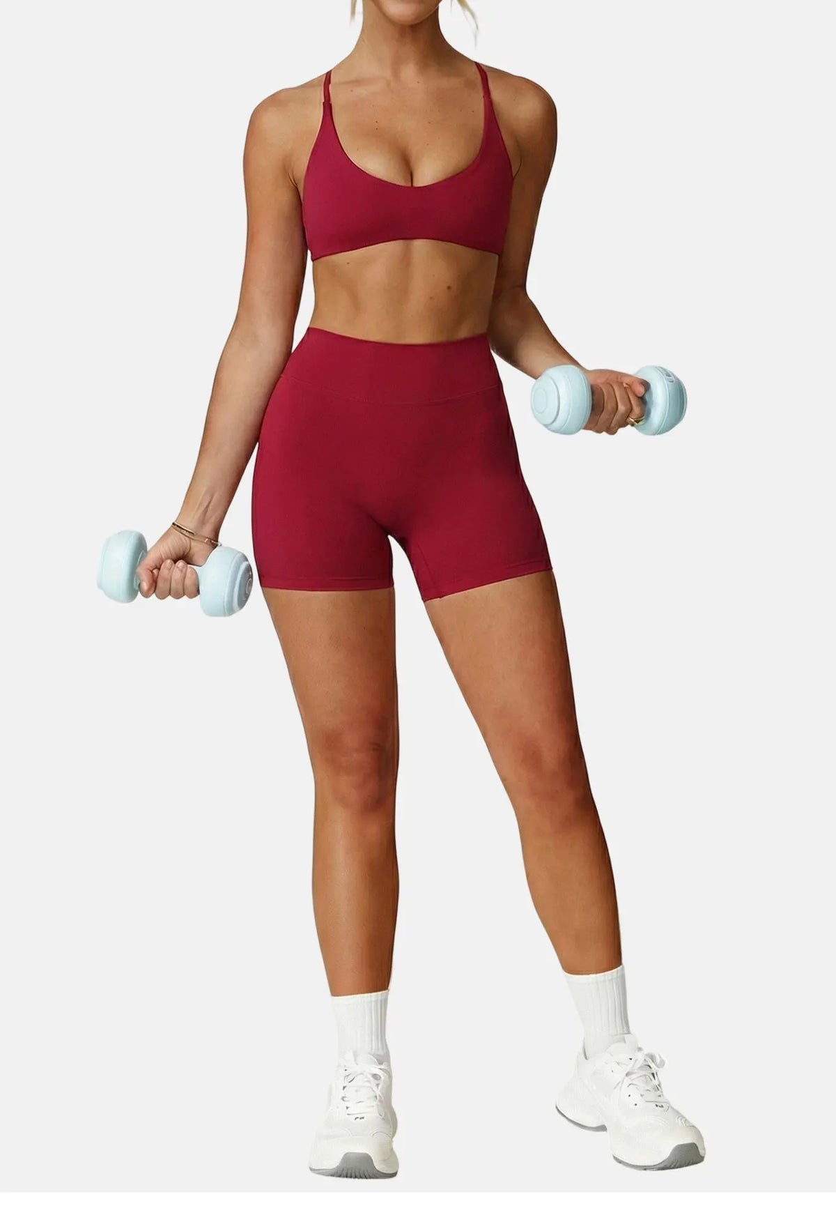 A woman wearing a maroon high-support sports bra and matching shorts, holding light dumbbells.