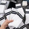Eine Hand hält einen Stapel atmungsaktiver weiß-schwarz gestreifter Socken auf einer dunkelgrauen Oberfläche.