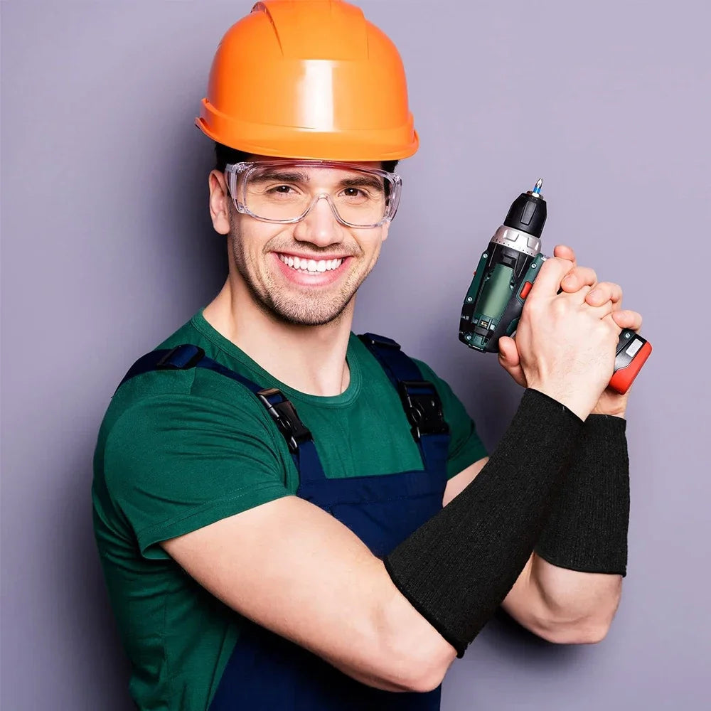 Lachender Mann mit Schutzbrille und orangem Schutzhelm hält ein grünes Werkzeug und schwarze Armschutzmanschetten.