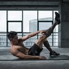 A muscular man wearing compression socks is performing a stretch or exercise indoors.