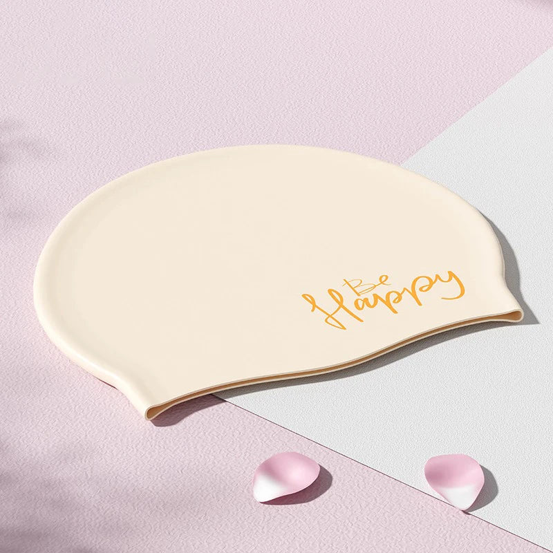 Gorra de silicona beige con la palabra Feliz escrita en dorado cursiva sobre un fondo rosa claro.