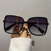 A hand holds a pair of black sunglasses with a two-tone gradient lens against a light background.