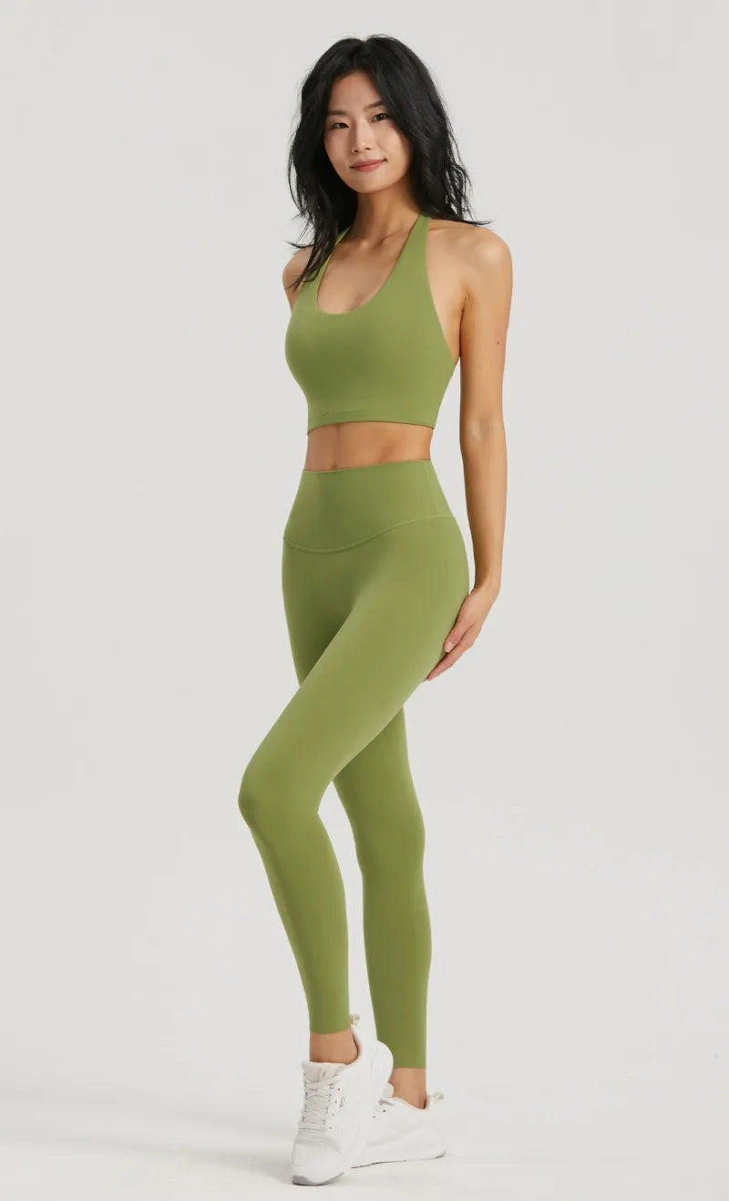 A woman models a olive green halter neck yoga and gym sports bra top and matching leggings.
