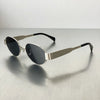 A pair of classic oval metal sunglasses with dark lenses and silver-toned arms resting on a gray surface.