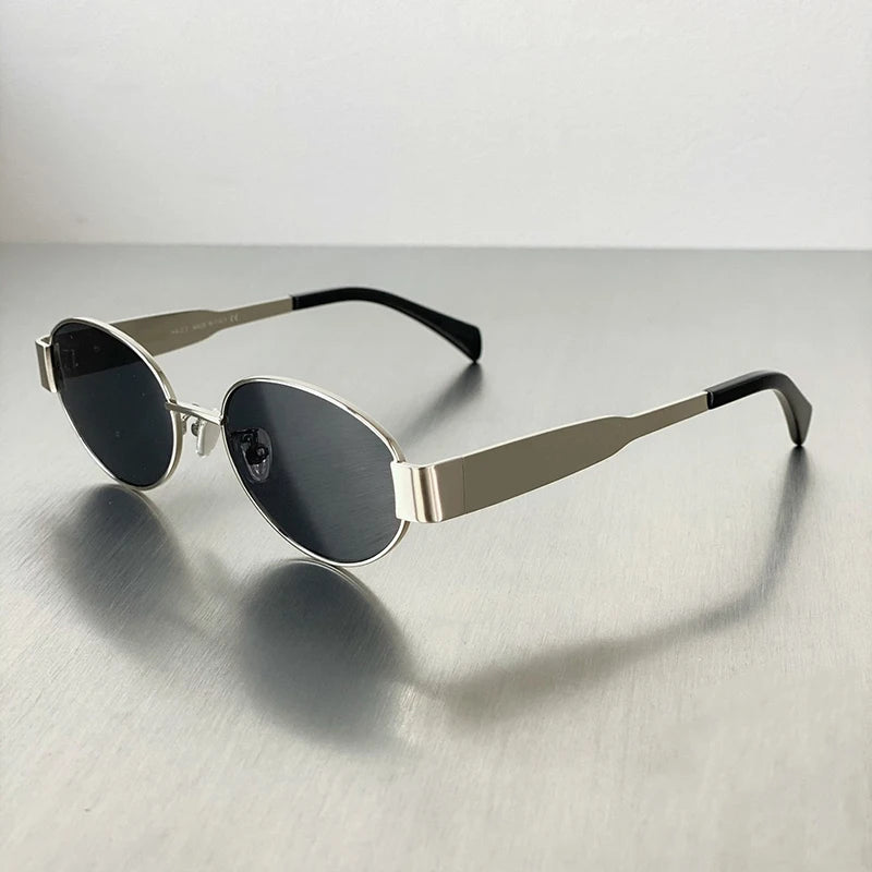 A pair of classic oval metal sunglasses with dark lenses and silver-toned arms resting on a gray surface.