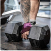 A person wearing purple wrist wraps is holding black gym wrist wraps on a dark surface.