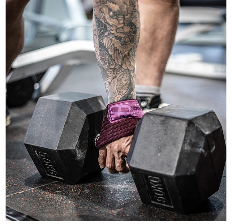 A person wearing purple wrist wraps is holding black gym wrist wraps on a dark surface.