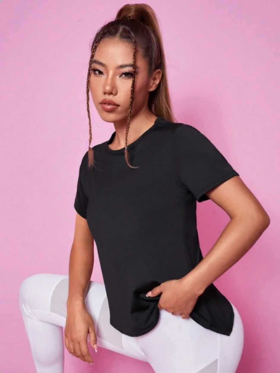 A woman models a black breathable summer yoga and fitness t-shirt in a studio setting.