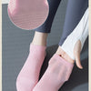 A pair of pink knitted yoga socks and a circular pink non-slip grip pad are shown on a gray surface.