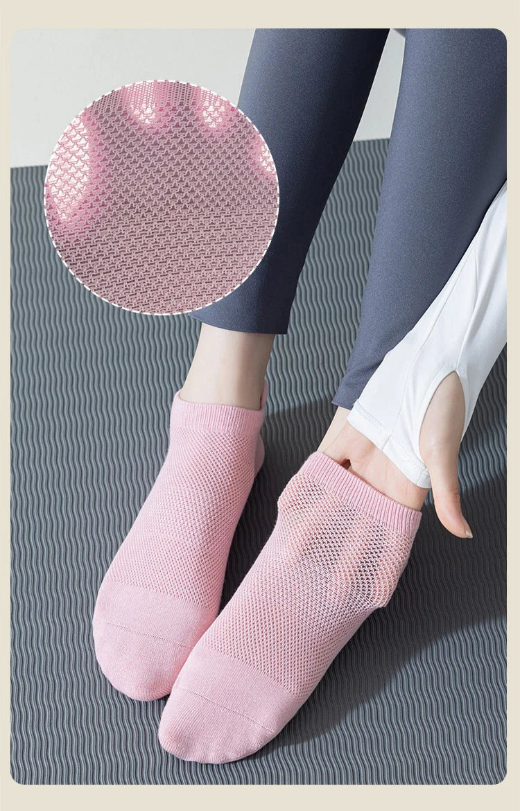 A pair of pink knitted yoga socks and a circular pink non-slip grip pad are shown on a gray surface.