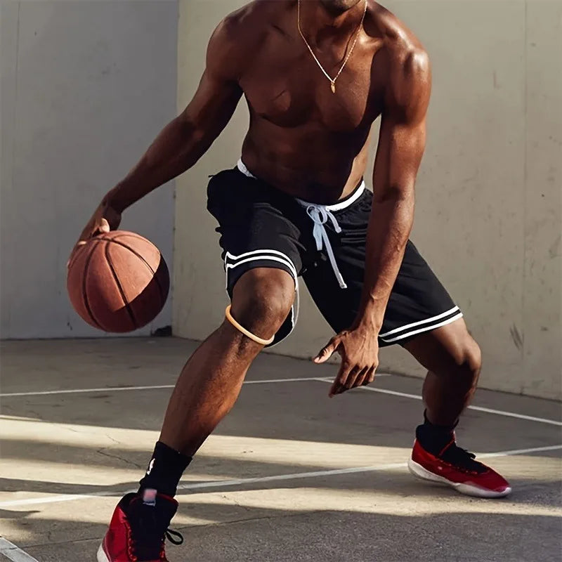 A muscular man wearing a black basketball shorts and a gold necklace is holding a basketball.