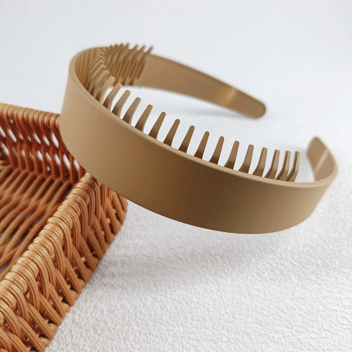 Beige Plastik-Haarband mit feinen Zähnen, das auf einem geflochtenen Korb liegt.