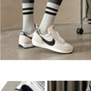 A person wearing black and white striped socks is shown standing on a gray surface next to a pair of Nike sneakers.