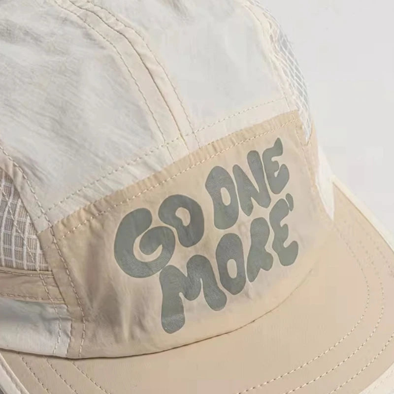 A close-up of a beige baseball cap with light gray text that reads GO ONE MORE