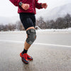 Eine Person läuft auf Asphalt, trägt eine schwarze Knieschiene und rote Sportkleidung.