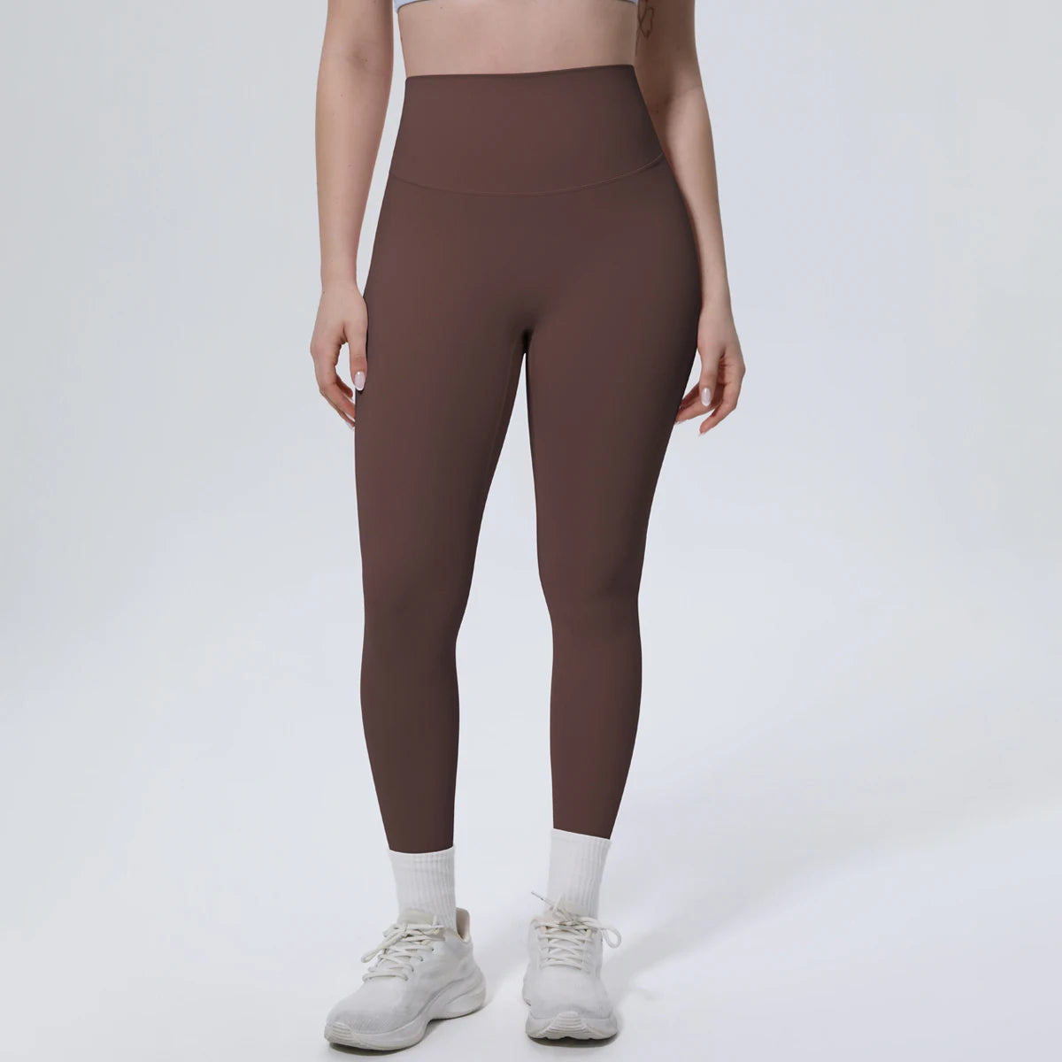 A model wearing high-waisted, dark brown quick-drying yoga and fitness leggings with white socks and light athletic shoes.