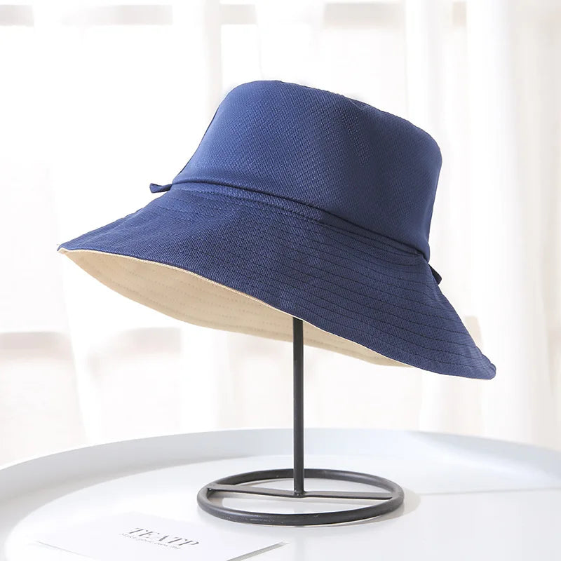 A navy blue double-sided wide brim bucket hat displayed on a stand.
