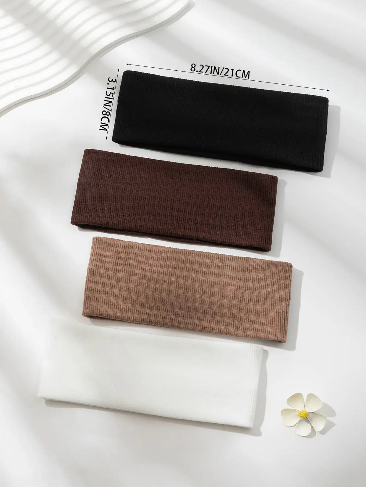 Un paquete de cuatro bandas elásticas para el cabello en negro, marrón, beige y blanco exhibidas sobre una superficie blanca.
