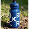 Botella de ciclismo azul y duradera de pie en tierra y hierba.