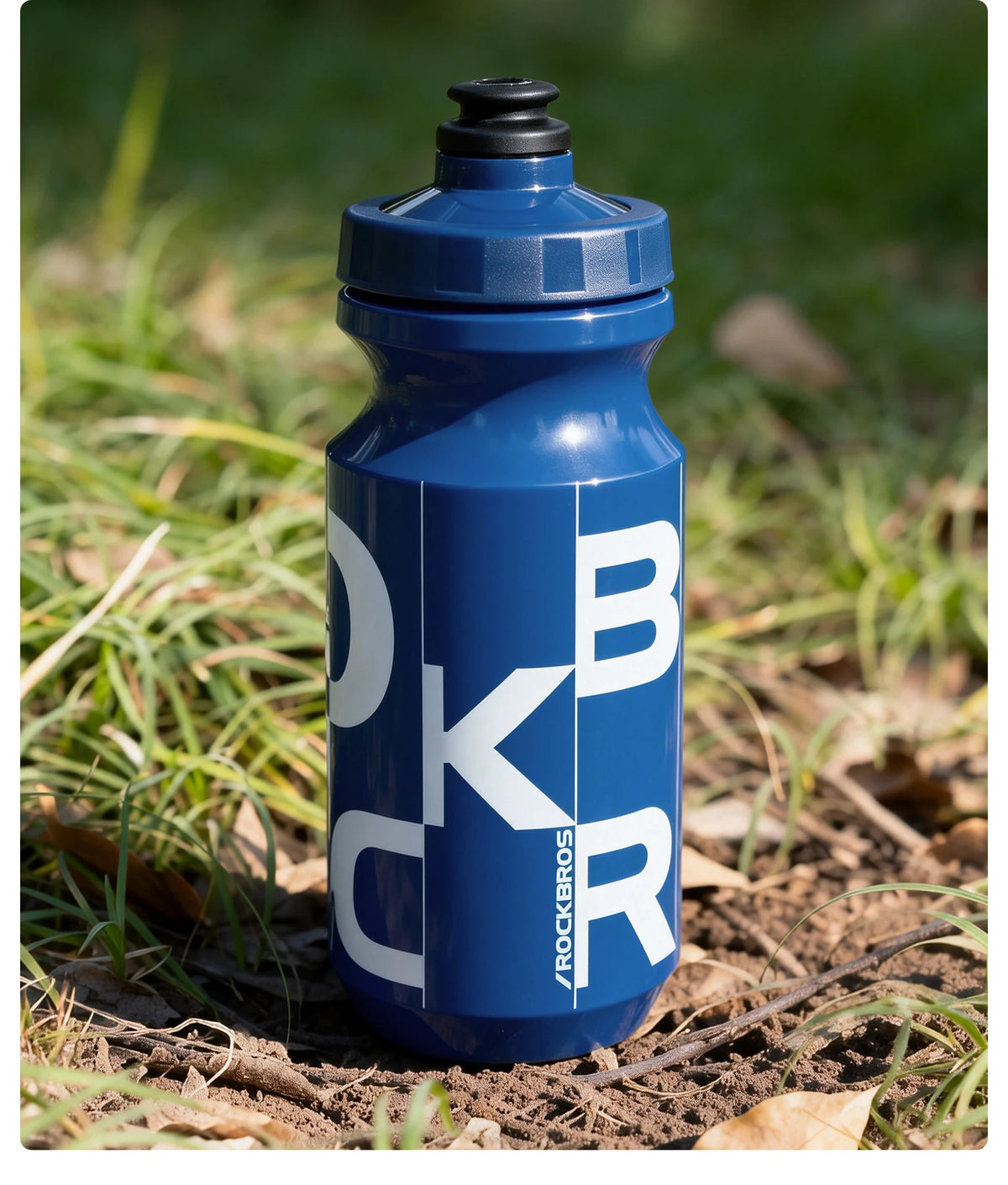 Botella de ciclismo azul y duradera de pie en tierra y hierba.