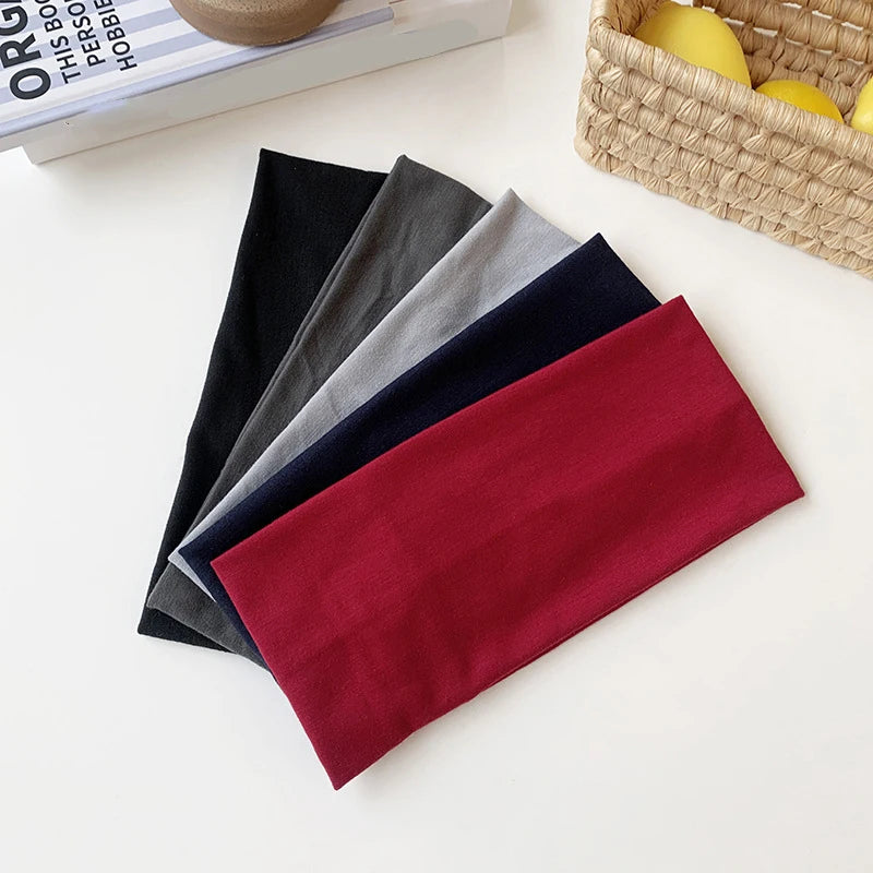 A stack of five elastic hairbands in various colors including black, gray, navy blue, and maroon, resting on a white surface.