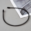 A black fashion metal hair band is shown against a light gray background next to a piece of paper.