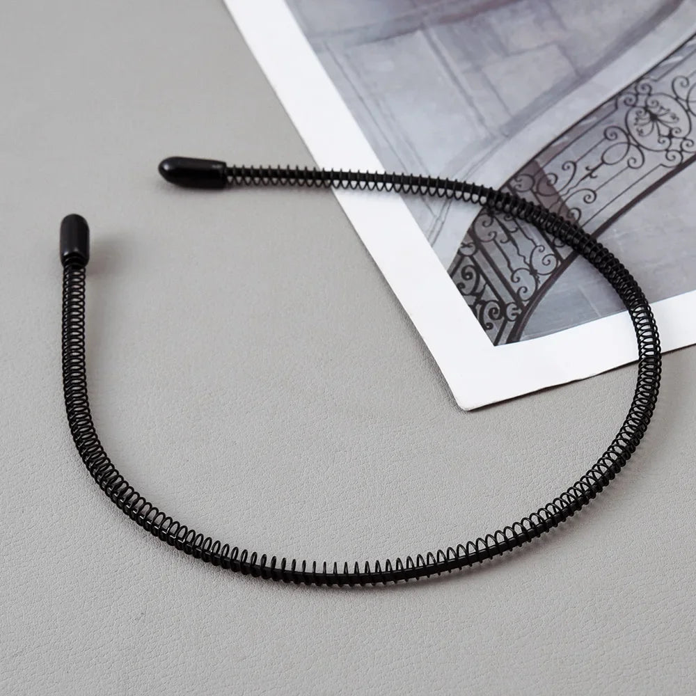 A black fashion metal hair band is shown against a light gray background next to a piece of paper.