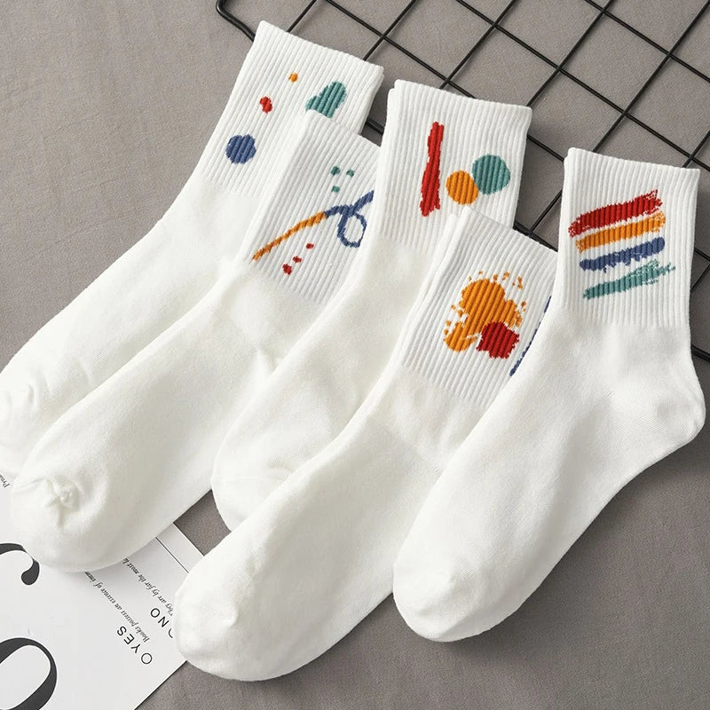 A stack of five white breathable cotton socks with colorful abstract designs laid on a gray surface.
