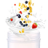 Ein weißer Proteinshake wird in eine klare Flasche gegossen, umgeben von verstreuten Beeren und Zitrusschalen.