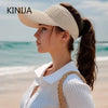 A woman wearing a white breathable anti-UV adjustable sun hat and a white top stands near the ocean.