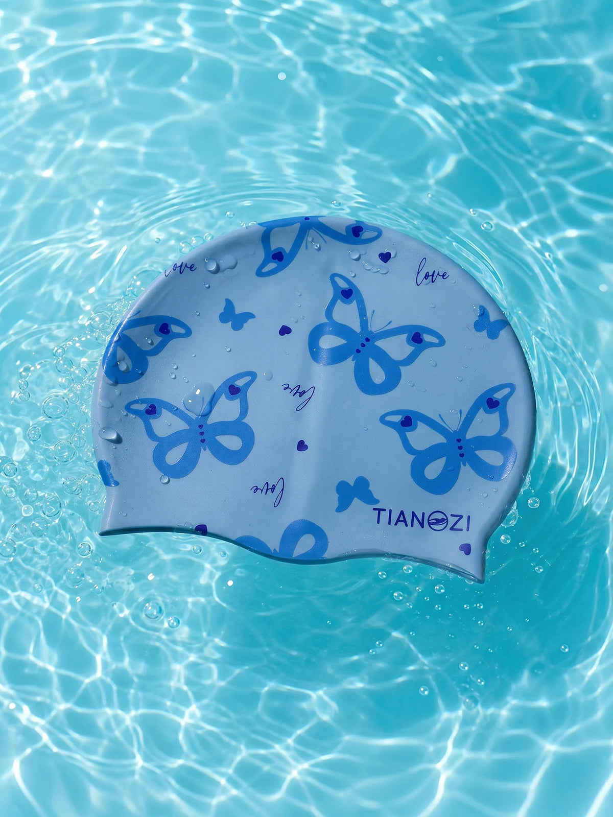A silicone swimming cap with a blue butterfly print floating in clear water.