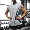 Muskulöser Mann in hellem grauem Tanktop und schwarzen Shorts im Fitnessstudio.