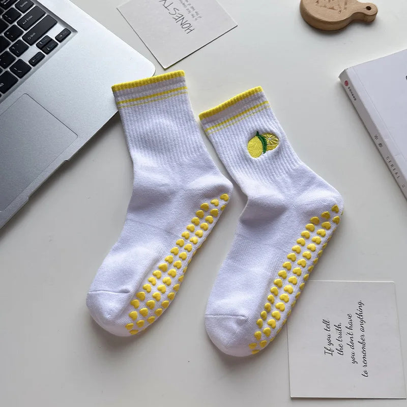 Paire de chaussettes de yoga blanches avec broderie jaune et adhérence antidérapante sur une surface blanche.