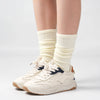 A pair of beige mid-calf yoga and pilates socks worn on a person's ankle and foot.