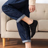 A person wearing dark blue denim jeans and black ankle socks sitting on a sofa.