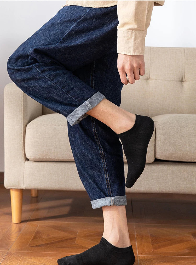 A person wearing dark blue denim jeans and black ankle socks sitting on a sofa.