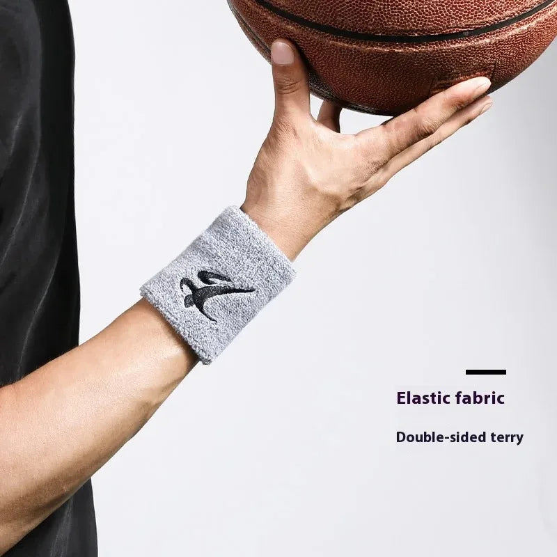 Eine Hand trägt ein graues elastisches Armband mit einem schwarzen Vogeldesign und hält einen braunen Basketball.