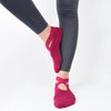 Un par de calcetines antideslizantes de color magenta intenso puestos en un pie, mostrados contra un fondo blanco.