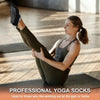 A woman wearing olive green yoga socks is performing a stretch on a wooden floor.