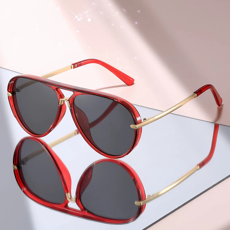 Red-framed aviator sunglasses with gold accents resting on a light pink surface.