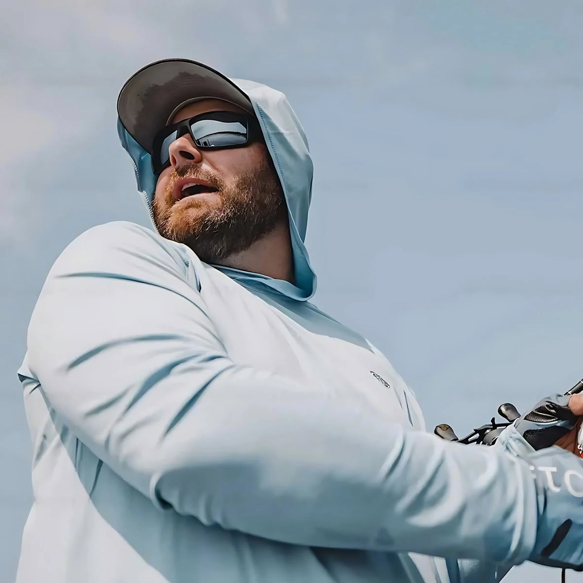 Ein Mann mit langem, hellblauem Hemd und Baseballkappe mit Sonnenbrille im Freien.