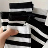 Eine Hand hält mehrere Paar atmungsaktive, schwarz-weiße gestreifte Socken hoch.