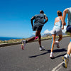 Three people run on a road with a railing under a clear blue sky.