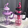 Two clear plastic drinking cups with pink and purple lids and black handles are displayed on a white surface.